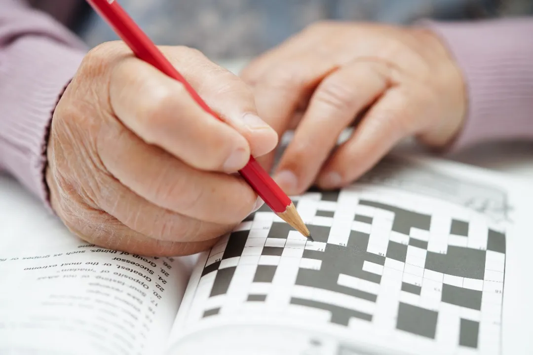 An elderly person engaged in cognitive activity such as crossword puzzles — maintaining mental stimulation is a key prevention strategy against dementia